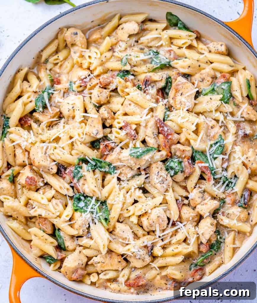 Top-down view of creamy Tuscan chicken pasta with fresh spinach and parmesan cheese in an orange skillet.