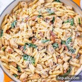 Top-down view of creamy chicken pasta with spinach in an orange skillet.