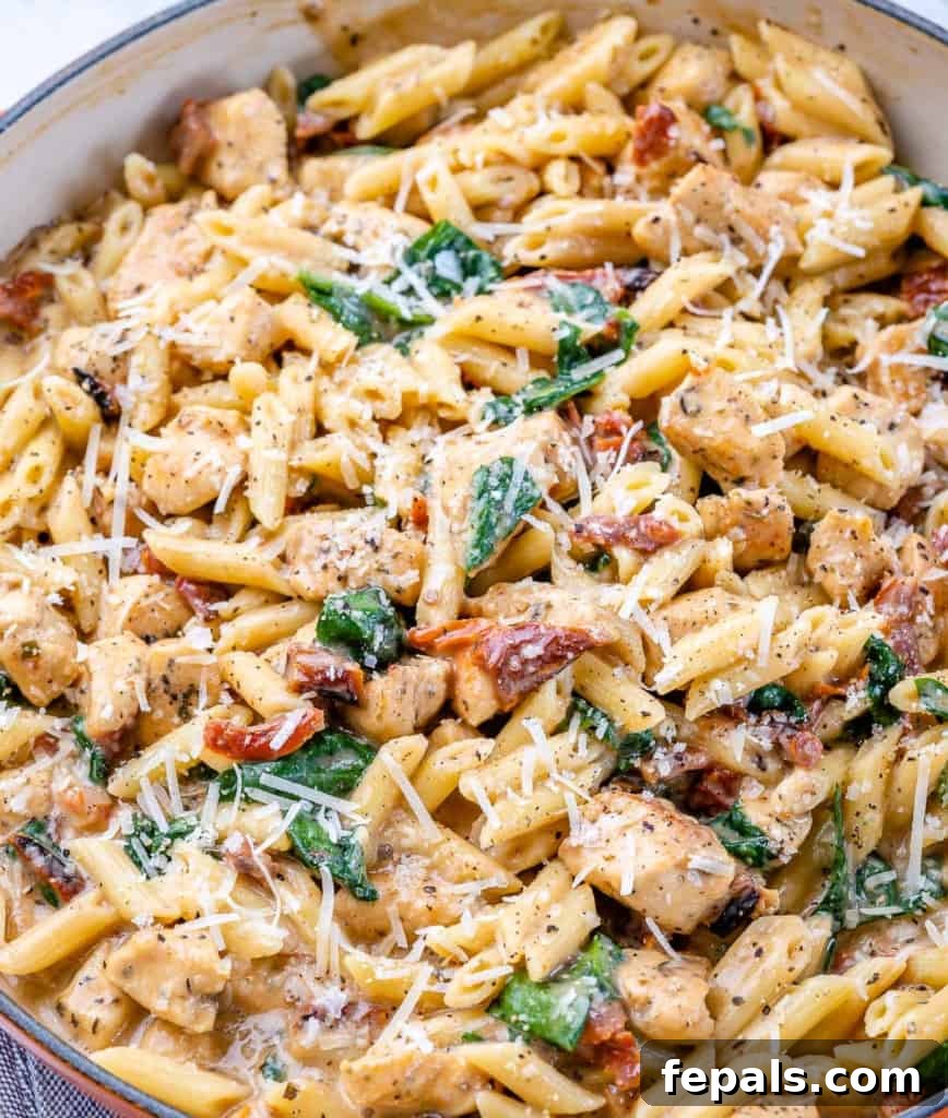 Close-up of creamy chicken pasta with spinach and parmesan cheese in a skillet, garnished with fresh herbs.