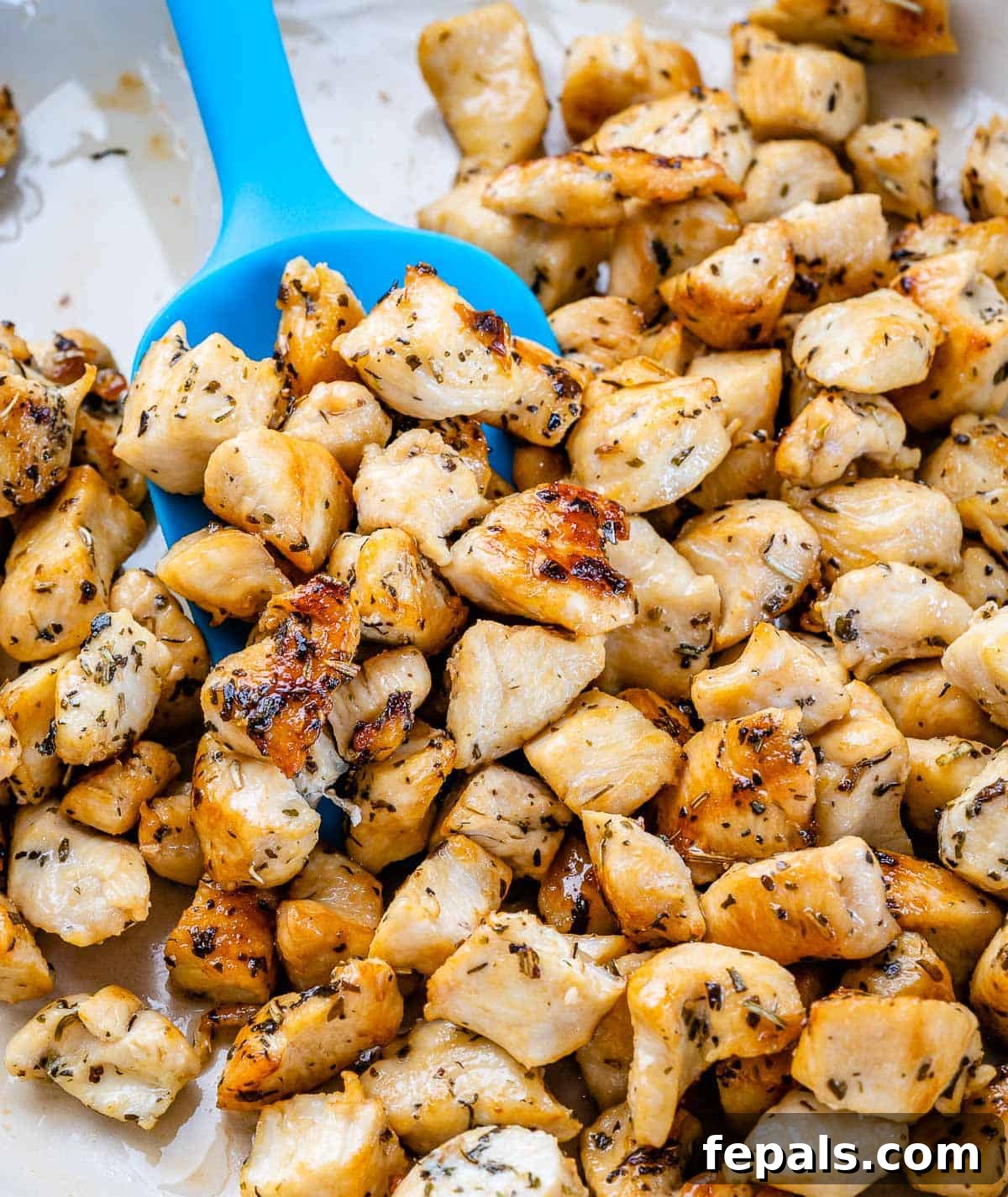 Cooked chicken bites seasoned and browned in a pan with a blue spatula.