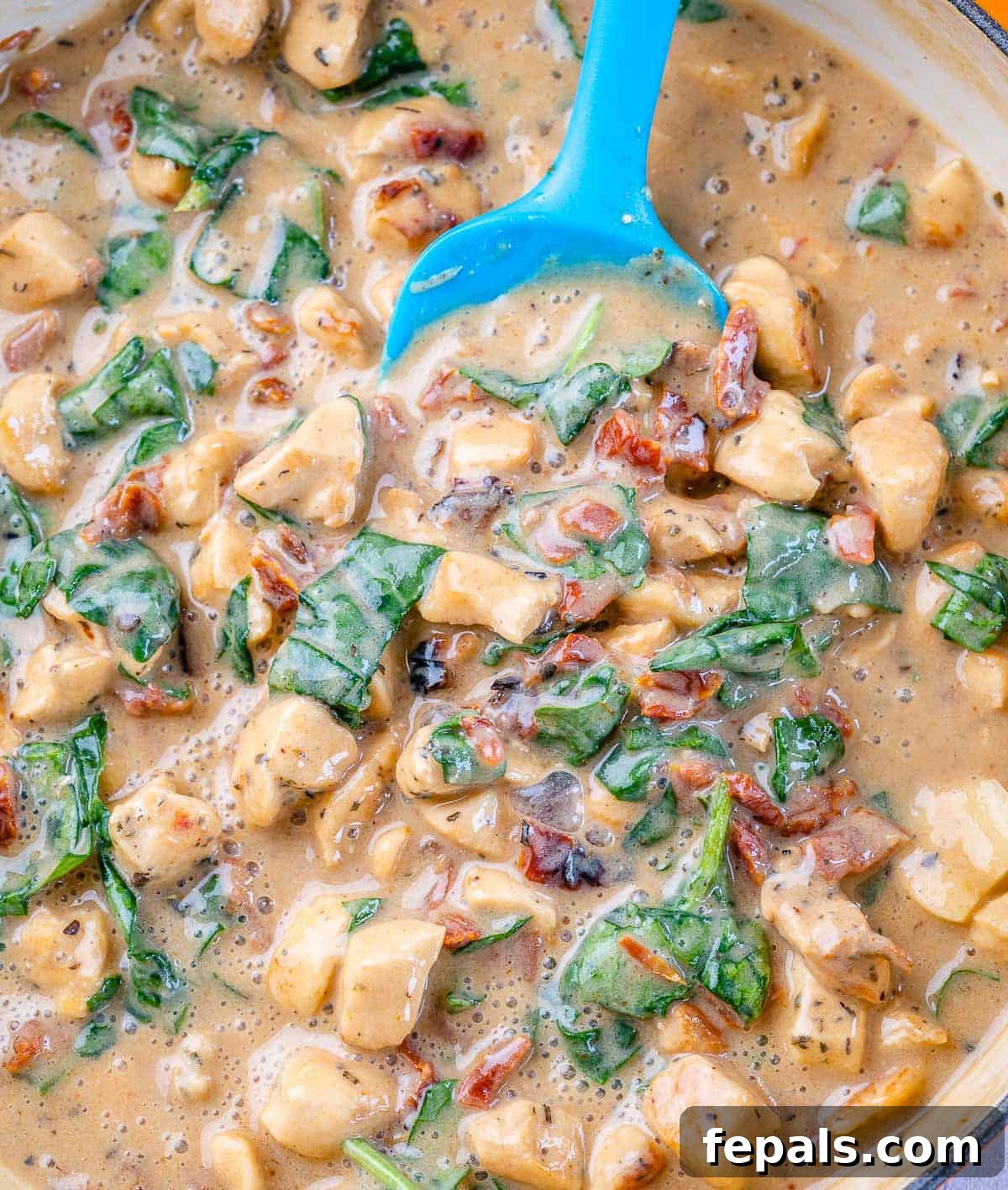 Creamy chicken sauce with wilted spinach, simmering in a skillet, ready for pasta.
