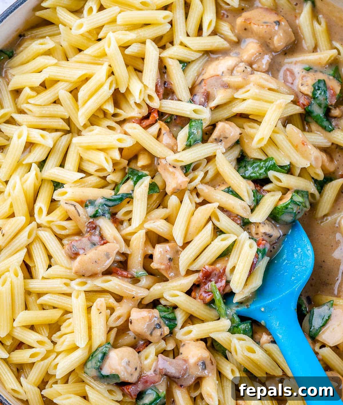 Cooked pasta being added to the creamy Tuscan chicken sauce in a skillet, ready to be combined.