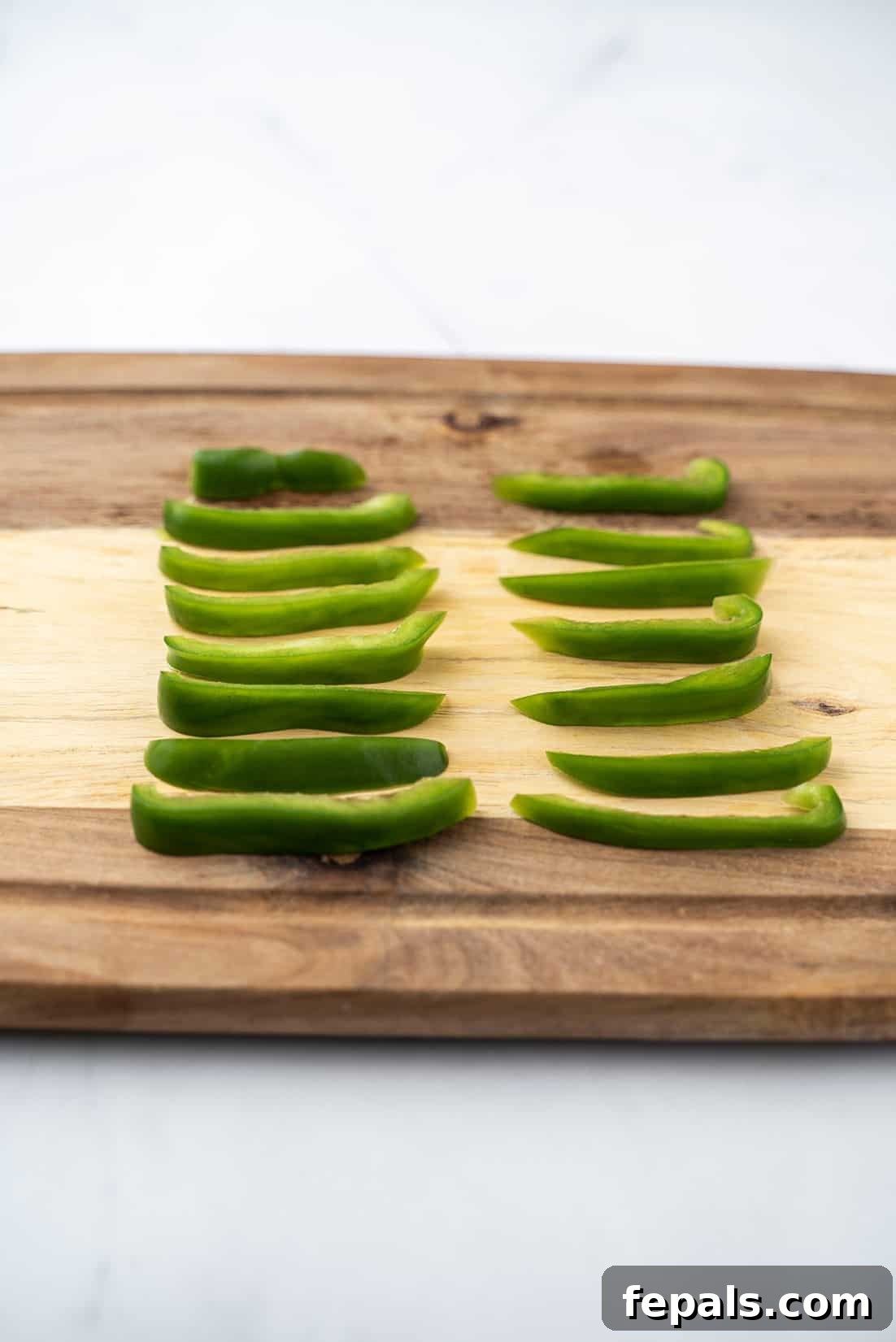 Master Bell Pepper Cutting Three Ways 11 Beautifully arranged vertical slices of various colored bell peppers on a wooden cutting board, highlighting their vibrant hues.