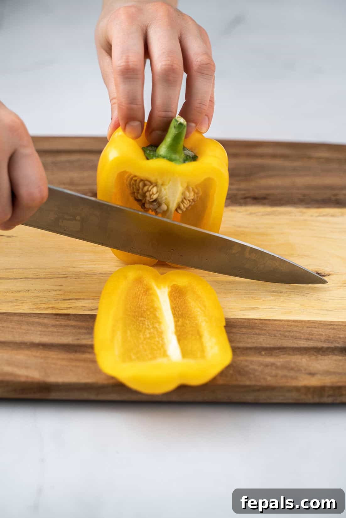 Master Bell Pepper Cutting Three Ways 12 Initial cut separating a vibrant yellow bell pepper side panel from the core using a sharp knife.