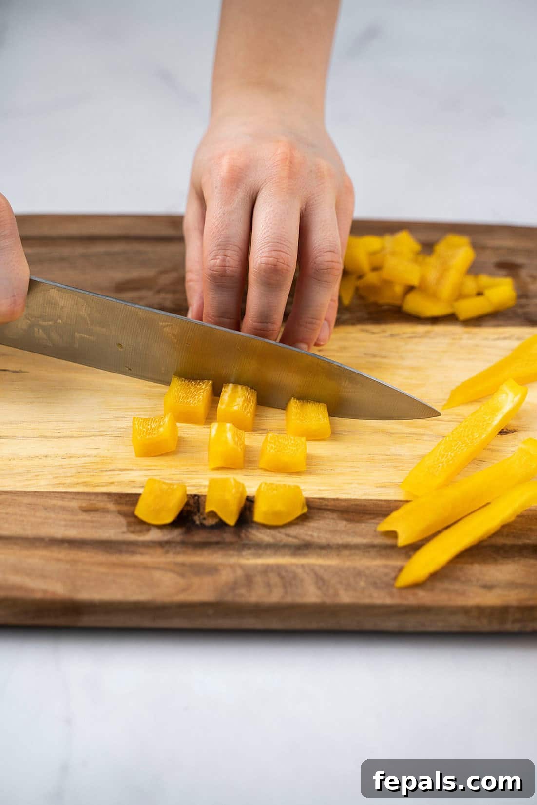Master Bell Pepper Cutting Three Ways 17 A hand skillfully cutting bell pepper slices into small, even cubes for consistent cooking.
