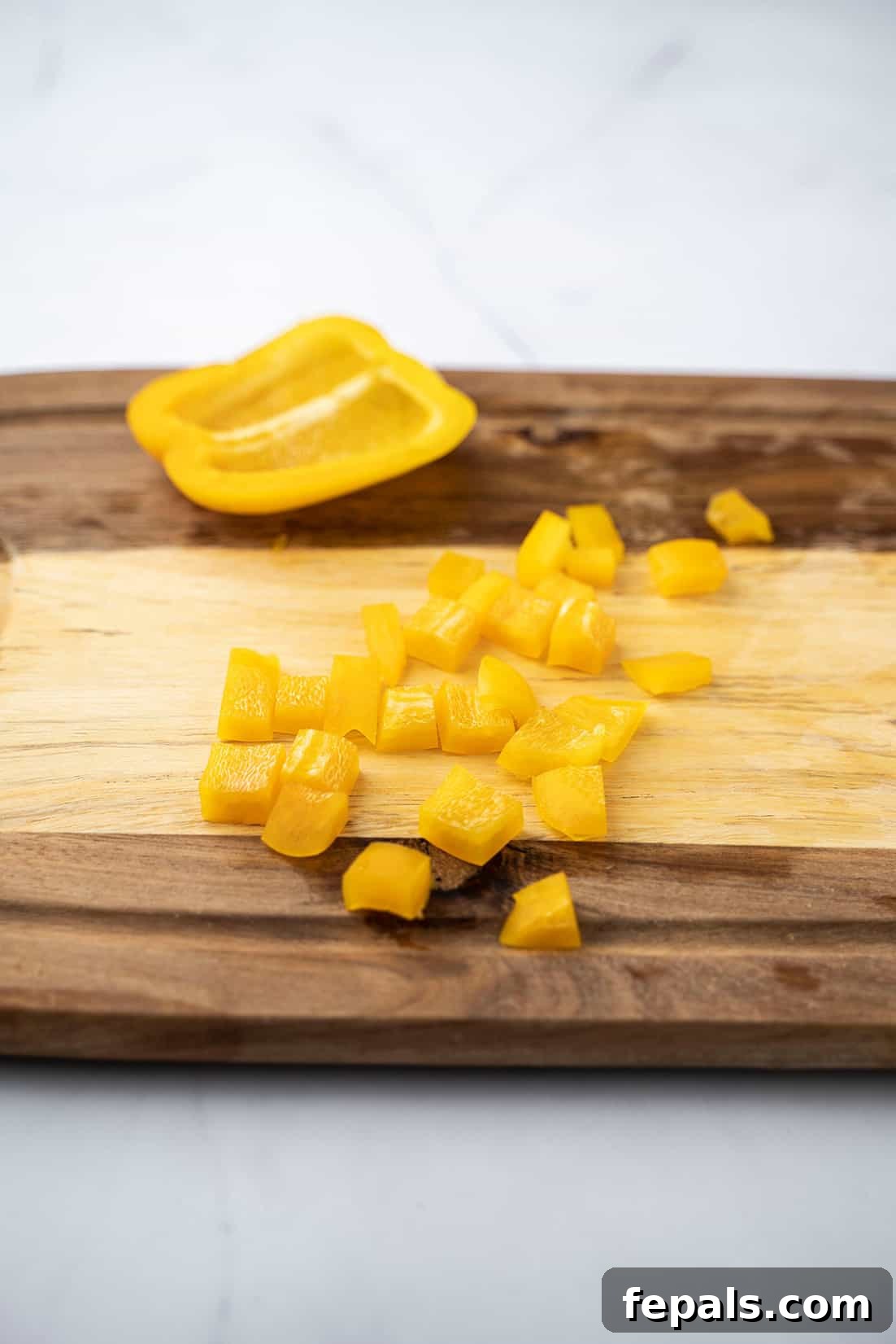 Master Bell Pepper Cutting Three Ways 18 A pile of uniformly cubed yellow bell peppers on a cutting board, ready for immediate use in cooking.