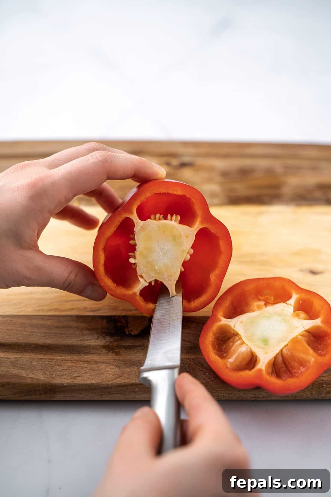 Master Bell Pepper Cutting Three Ways 20 A knife is used to carefully remove the seeds and white inner parts of a bell pepper, leaving a clean cavity.