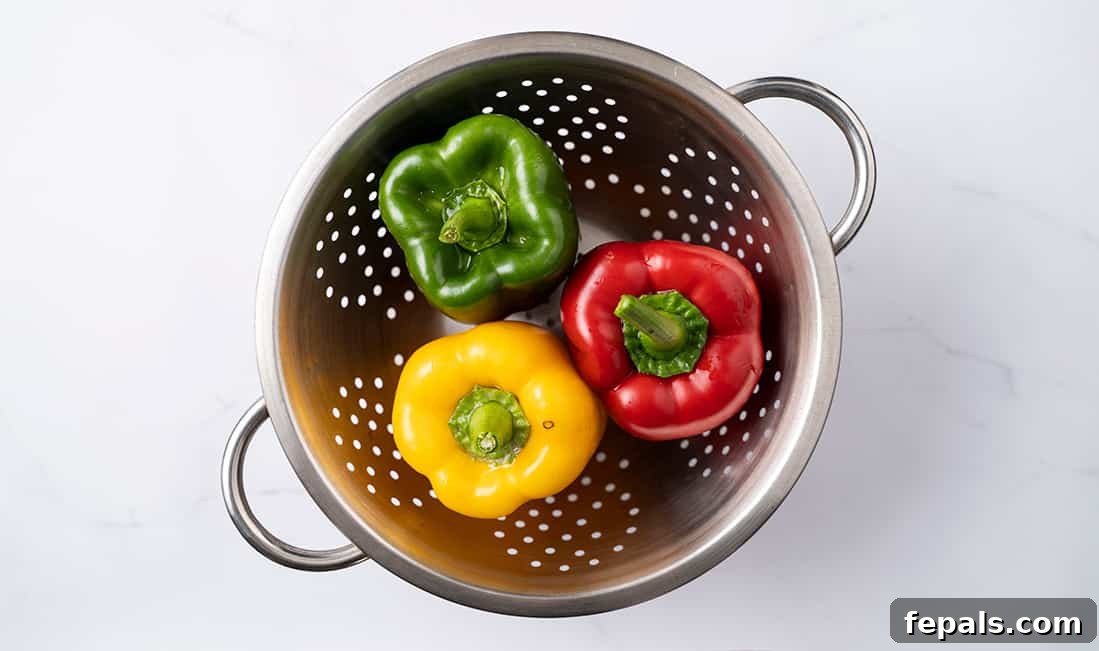 Master Bell Pepper Cutting Three Ways 3 Three vividly colored bell peppers (red, yellow, green) neatly arranged in a colander, freshly washed and ready for preparation.
