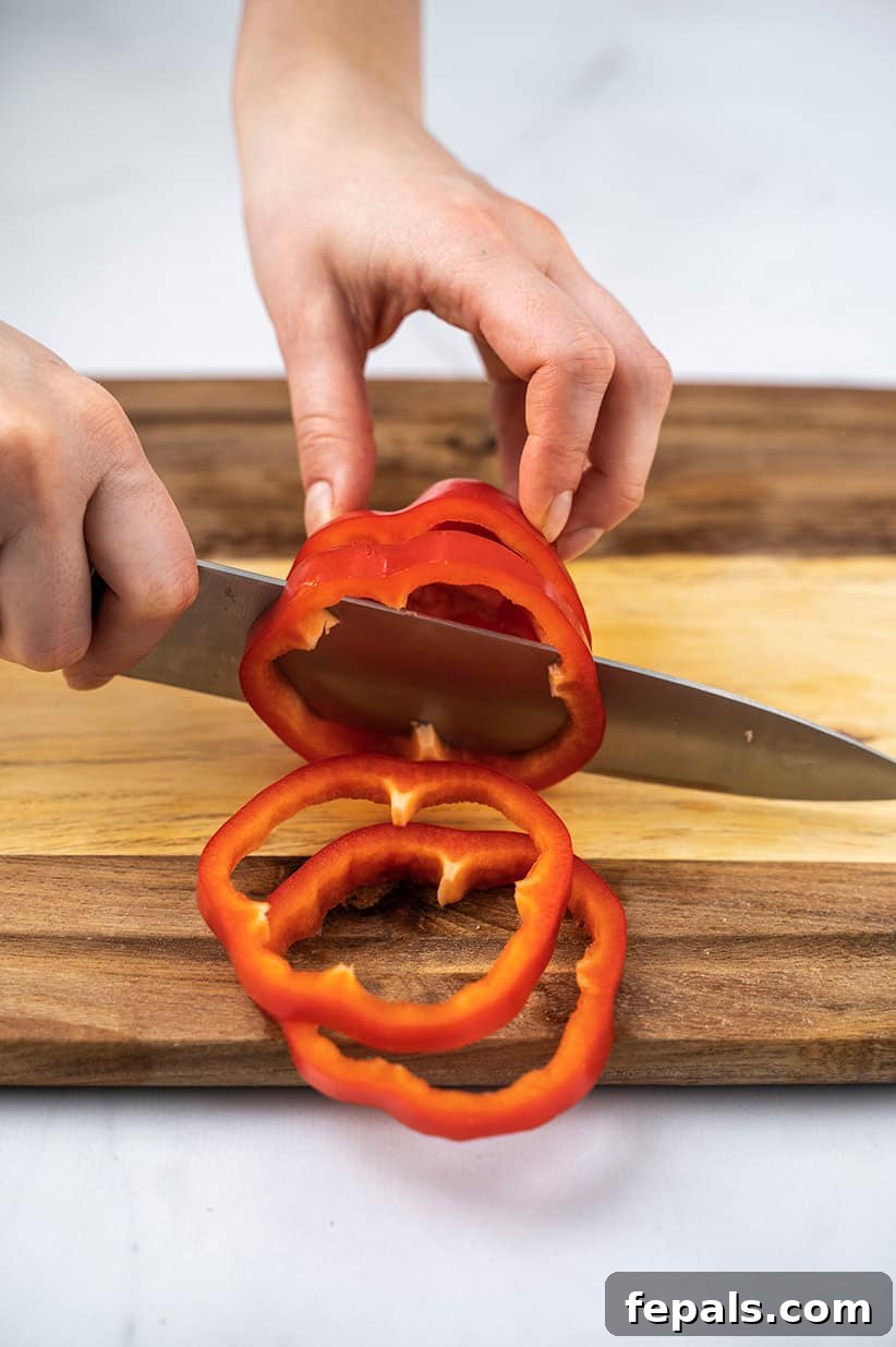 Master Bell Pepper Cutting Three Ways 21 A hand firmly holding a bell pepper while a knife slices it into perfect, even rings, ready for use.