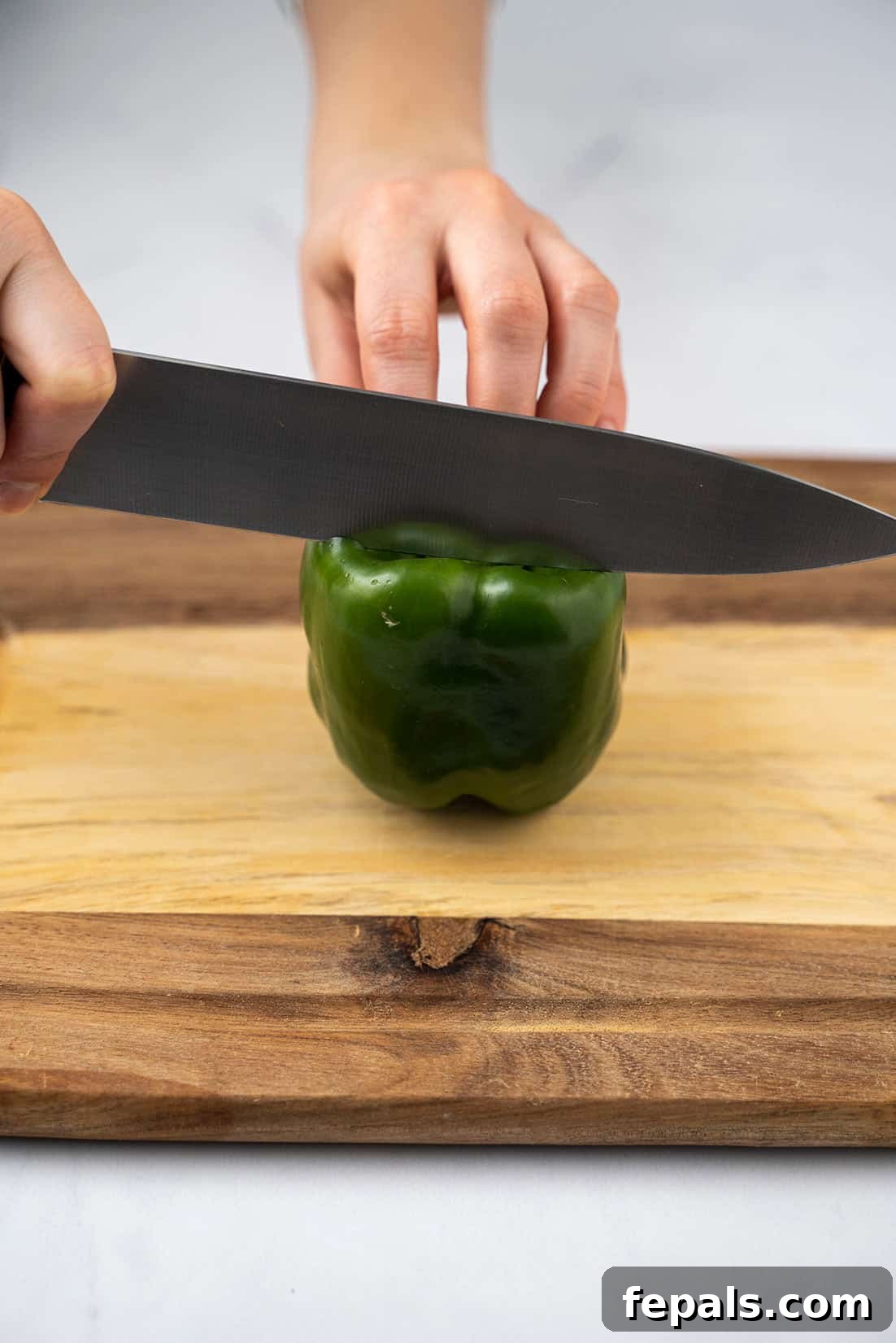 Master Bell Pepper Cutting Three Ways 5 Initial slice separating a side panel from a green bell pepper, keeping the core intact.
