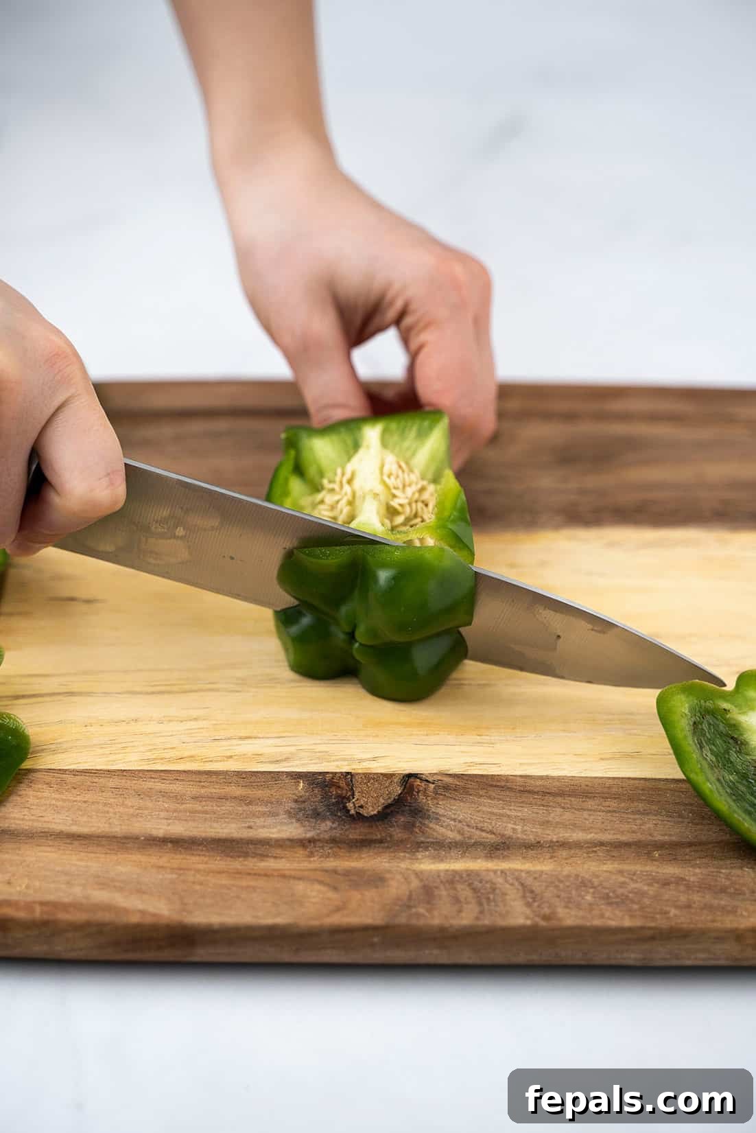 Master Bell Pepper Cutting Three Ways 7 Carefully slicing off the bottom section of a green bell pepper, ensuring a clean cut and minimal waste.