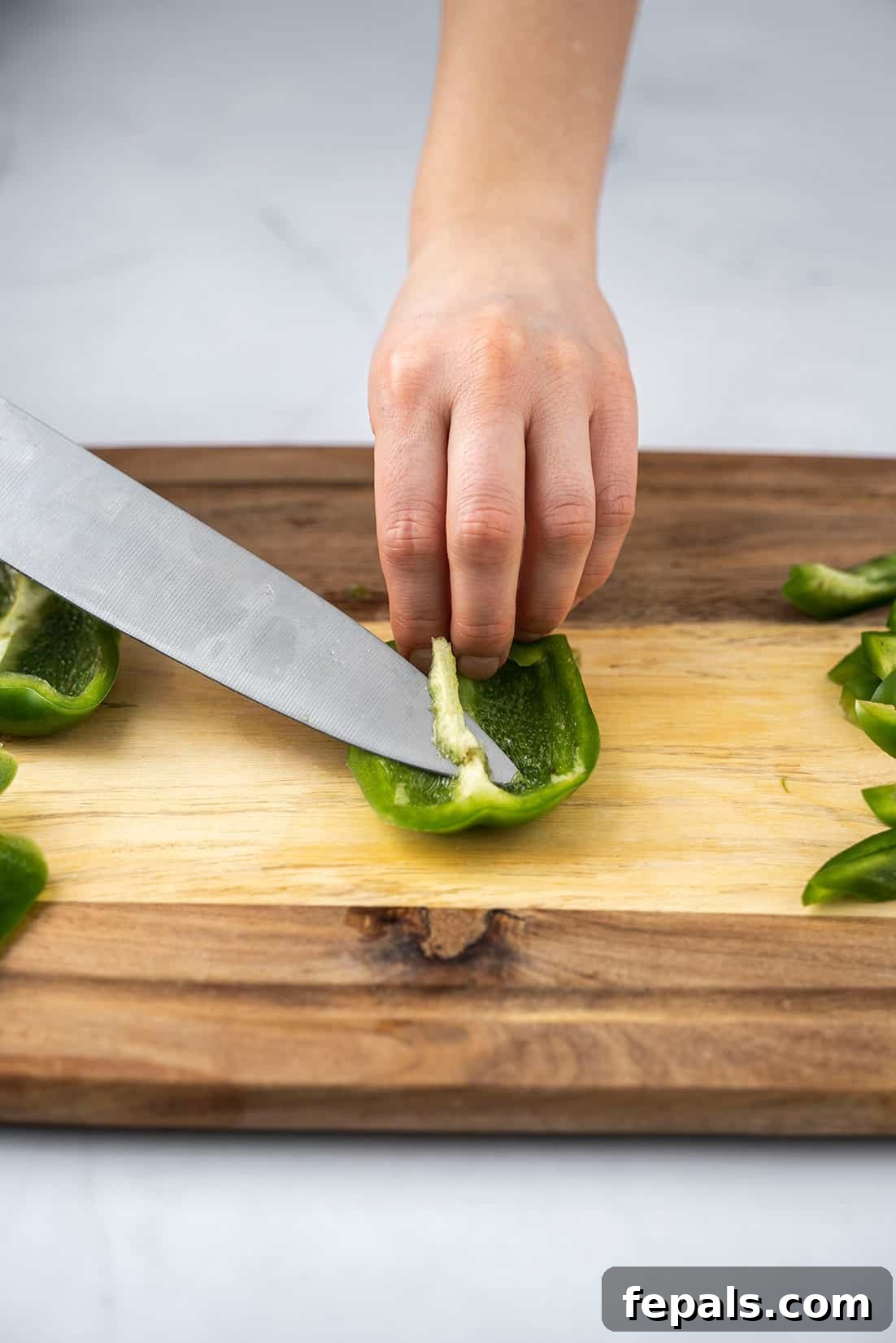 Master Bell Pepper Cutting Three Ways 9 Using a knife to meticulously remove all seeds and white membranes from the inside of a bell pepper section.