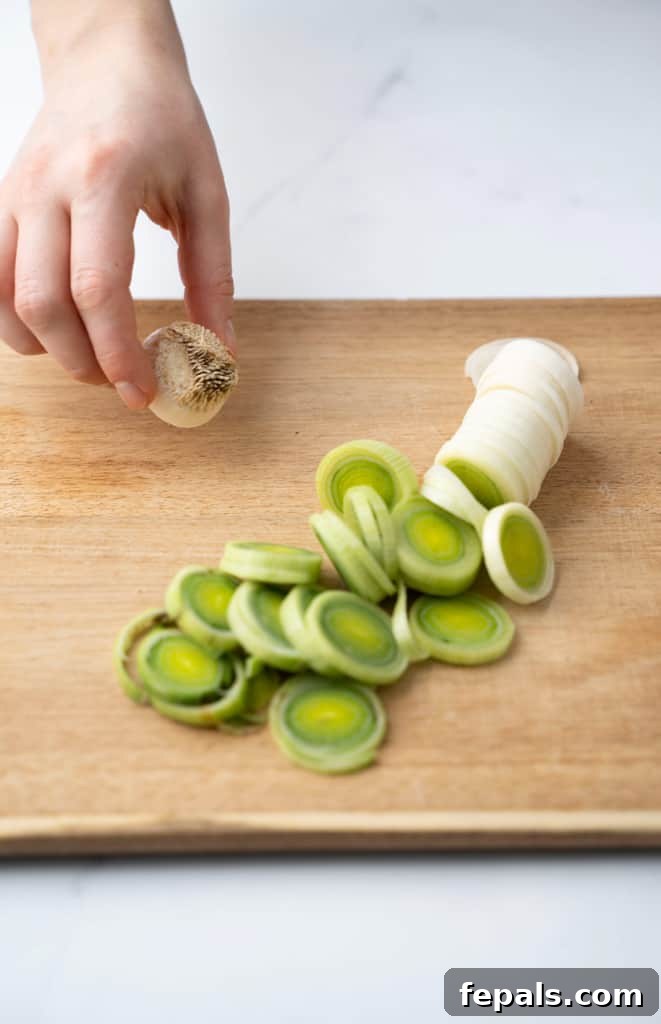 Mastering Leek Slicing 8 Cut leek pieces on a cutting board with a hand holding the root.
