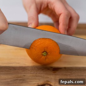 Side shot image of a knife slicing the top of an orange, illustrating the prep step.