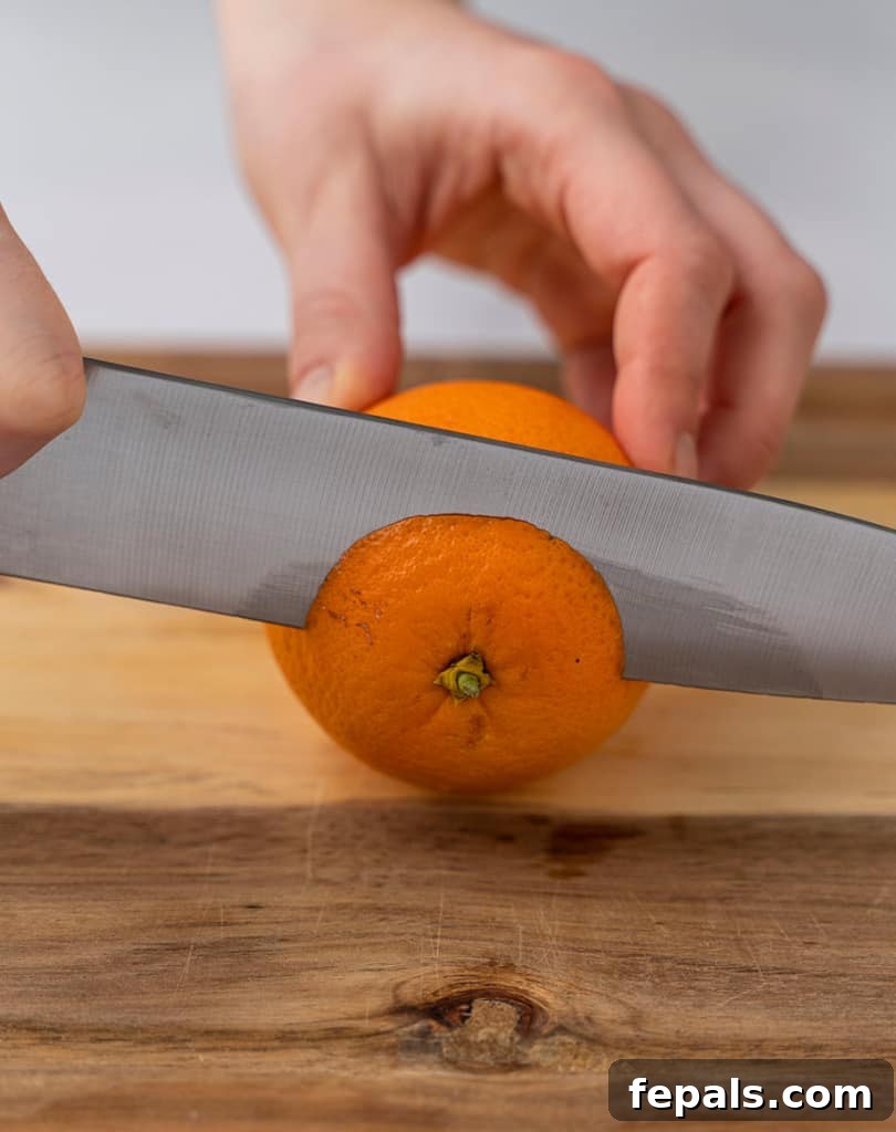 Side shot image of a knife slicing the top of an orange, preparing it for peeling.