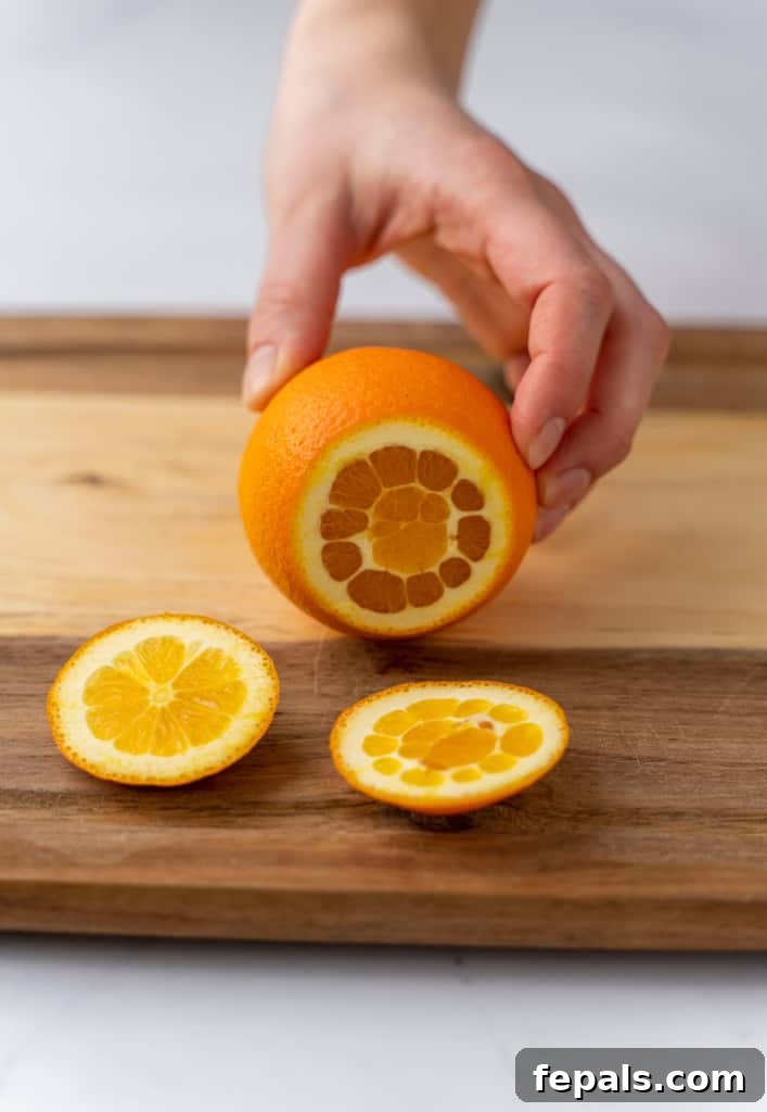 Side shot of the top of the orange being sliced off, exposing the fruit inside.