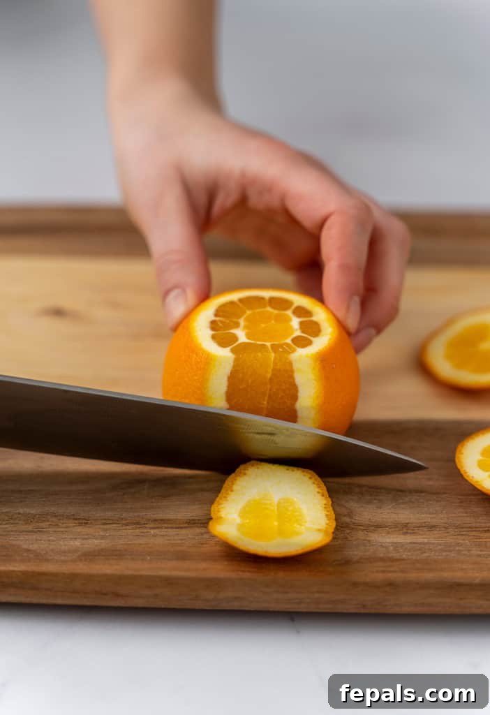 The side of the orange peel being sliced off in a continuous strip, revealing the fruit.