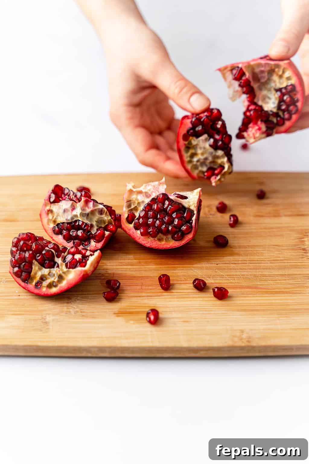 How to Cut a Pomegranate A pomegranate being deseeded and split into further pieces on a cutting board.