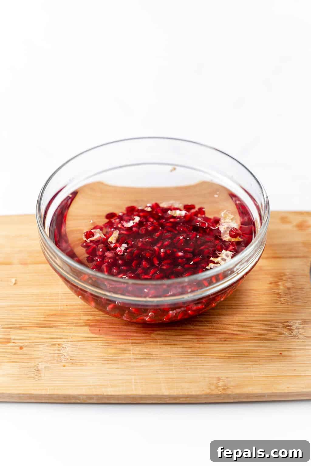 How to Cut a Pomegranate A bowl of water with pomegranate seeds submerged and pith floating on top.