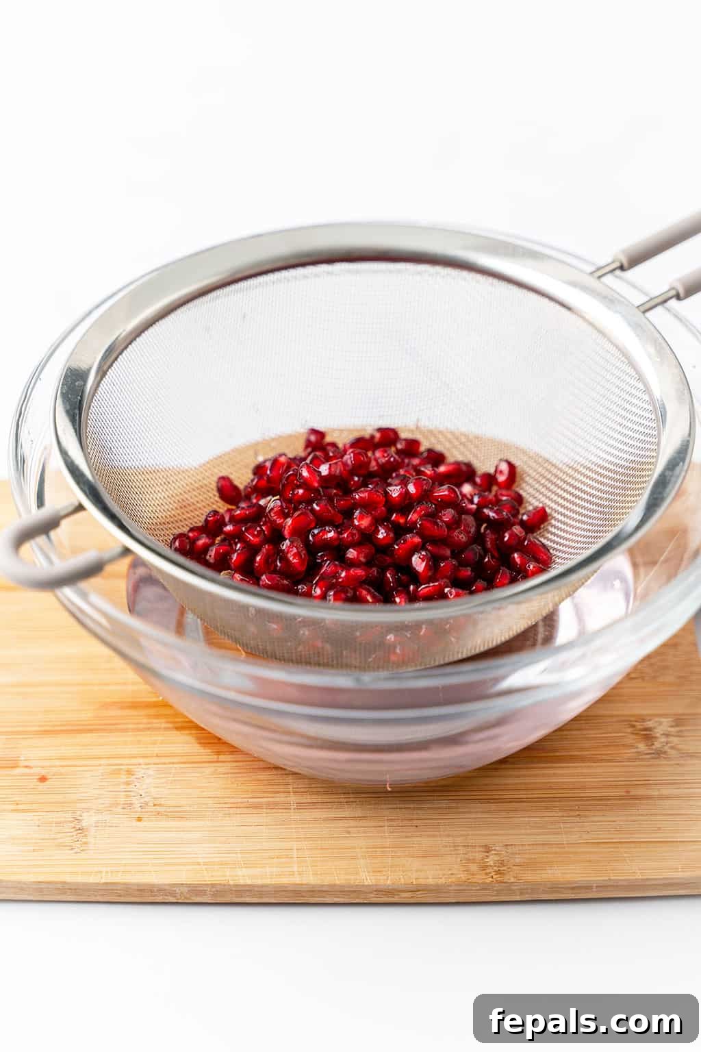 How to Cut a Pomegranate Clean pomegranate arils being rinsed in a mesh strainer over a bowl of water.
