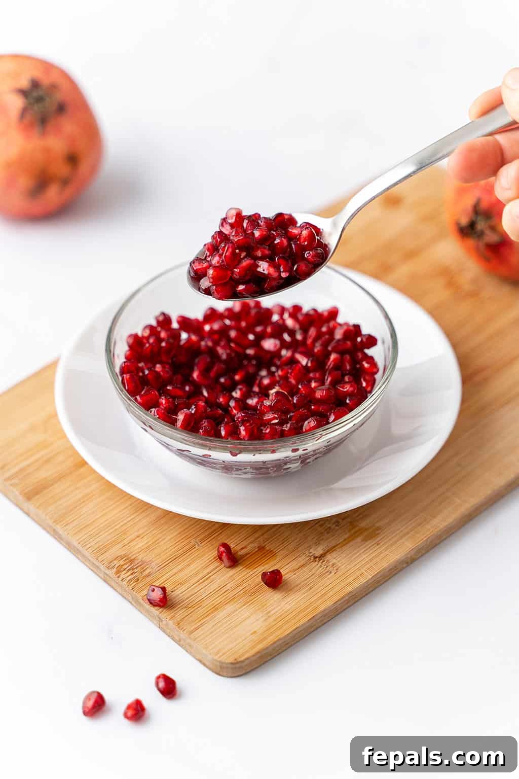 How to Cut a Pomegranate A glistening bowl filled with fresh pomegranate arils, with a spoon showcasing their beauty.