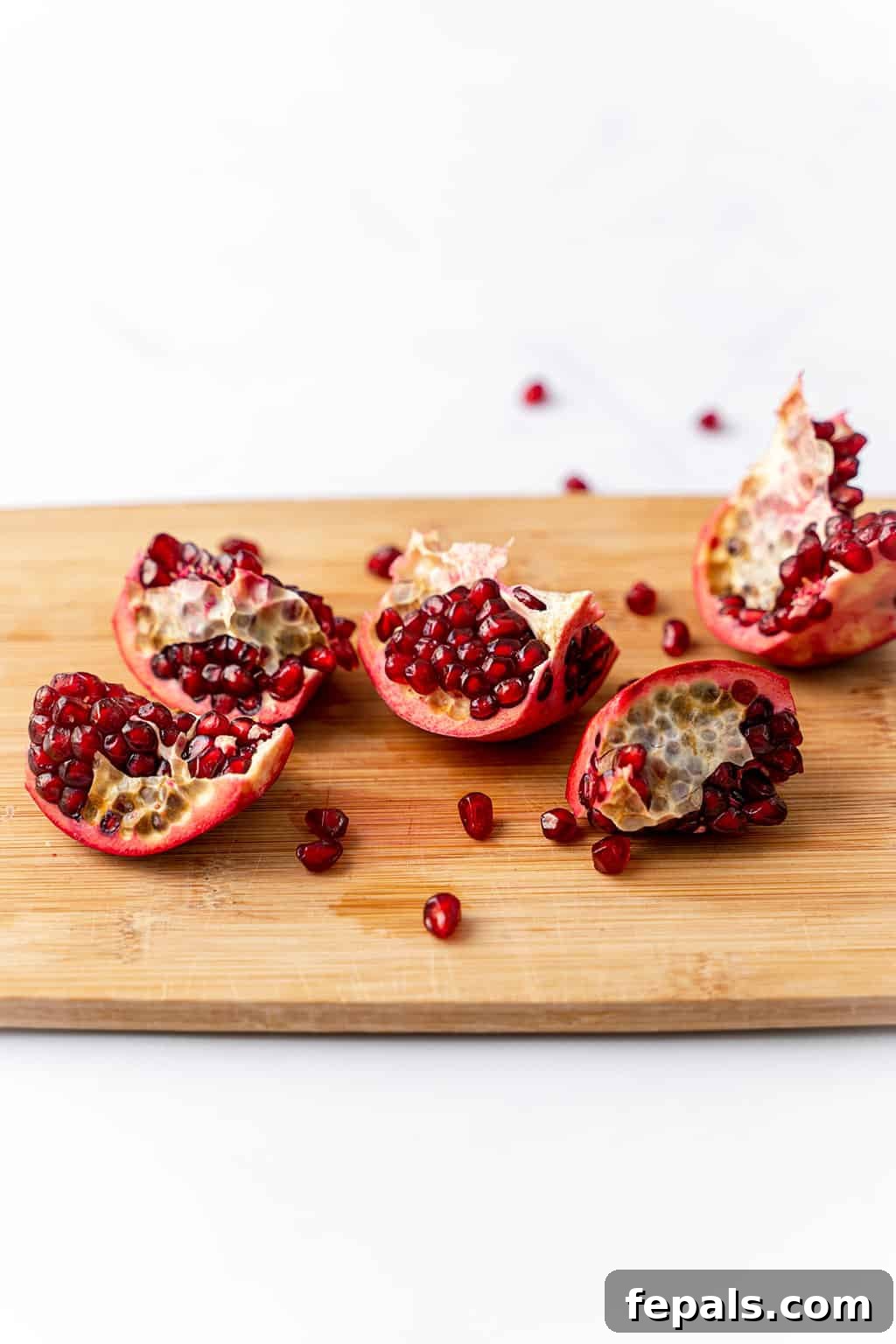 How to Cut a Pomegranate Segments of a cut pomegranate, with some arils already removed, laid out on a wooden cutting board.