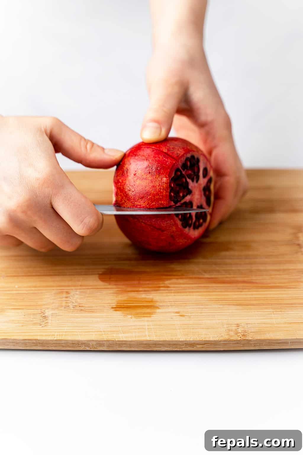 How to Cut a Pomegranate A knife scoring the pomegranate skin along its natural ridge on a cutting board.