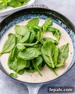 spinach added in a creamy sauce in a pan.