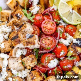 Close-up view of a grilled chicken salad featuring juicy tomatoes and tender chicken pieces.