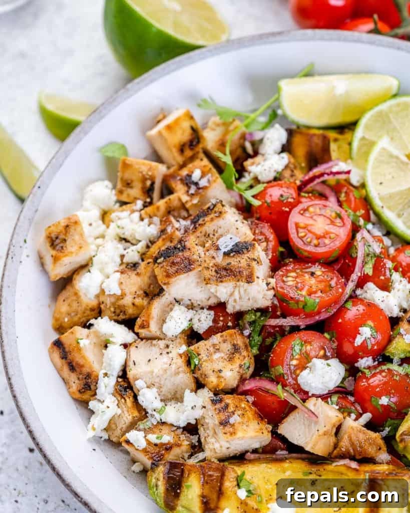 Close-up view of a vibrant grilled chicken avocado salad, adorned with fresh limes and red onion slices.