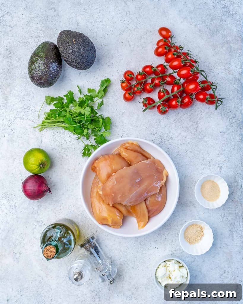 A vibrant display of fresh ingredients: chicken breasts, cherry tomatoes, cilantro, lime wedges, red onion, olive oil, salt, pepper, crumbled feta cheese, garlic powder, and onion powder, ready for a grilled avocado chicken salad.