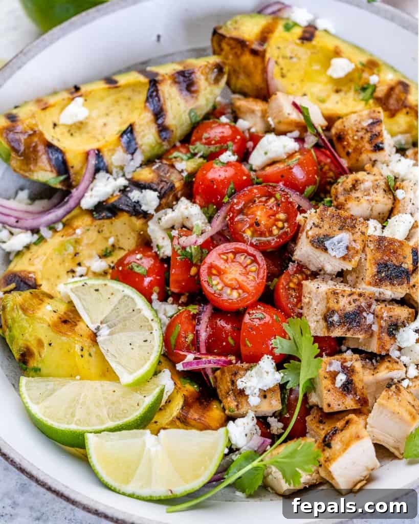 A beautiful bowl of grilled avocado chicken salad, generously topped with juicy cherry tomatoes and crumbled feta cheese.