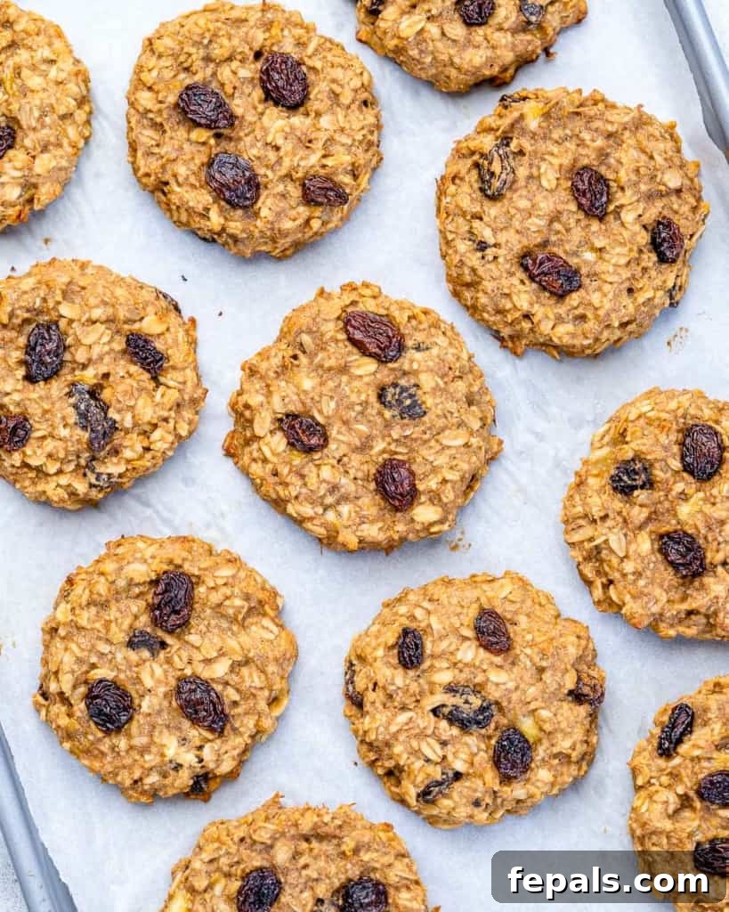 Chewy Raisin Oat Delights 8 Top down view of freshly baked oatmeal raisin cookies cooling on a wire rack on a baking sheet, with a single ripe banana beside it.