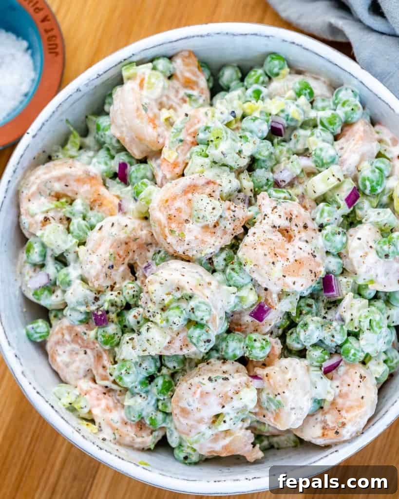 Refreshing Shrimp Salad 2 Top view of a creamy shrimp salad with peas and celery in a white bowl, garnished with fresh herbs