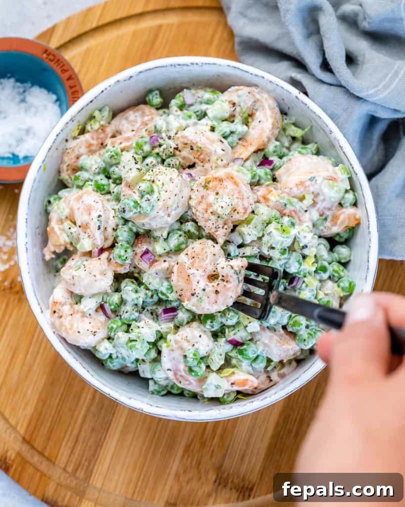 Refreshing Shrimp Salad 8 A hand holding a black fork, scooping into a bowl of creamy shrimp salad.