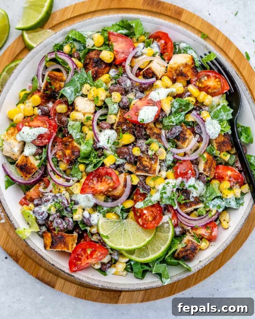 Fiesta Grilled Chicken Salad 2 Top view of a vibrant Mexican grilled chicken salad in a white plate with a black fork, set on a brown wooden board.