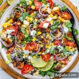 top view of chicken salad in a white plate with black fork in it over a brown board