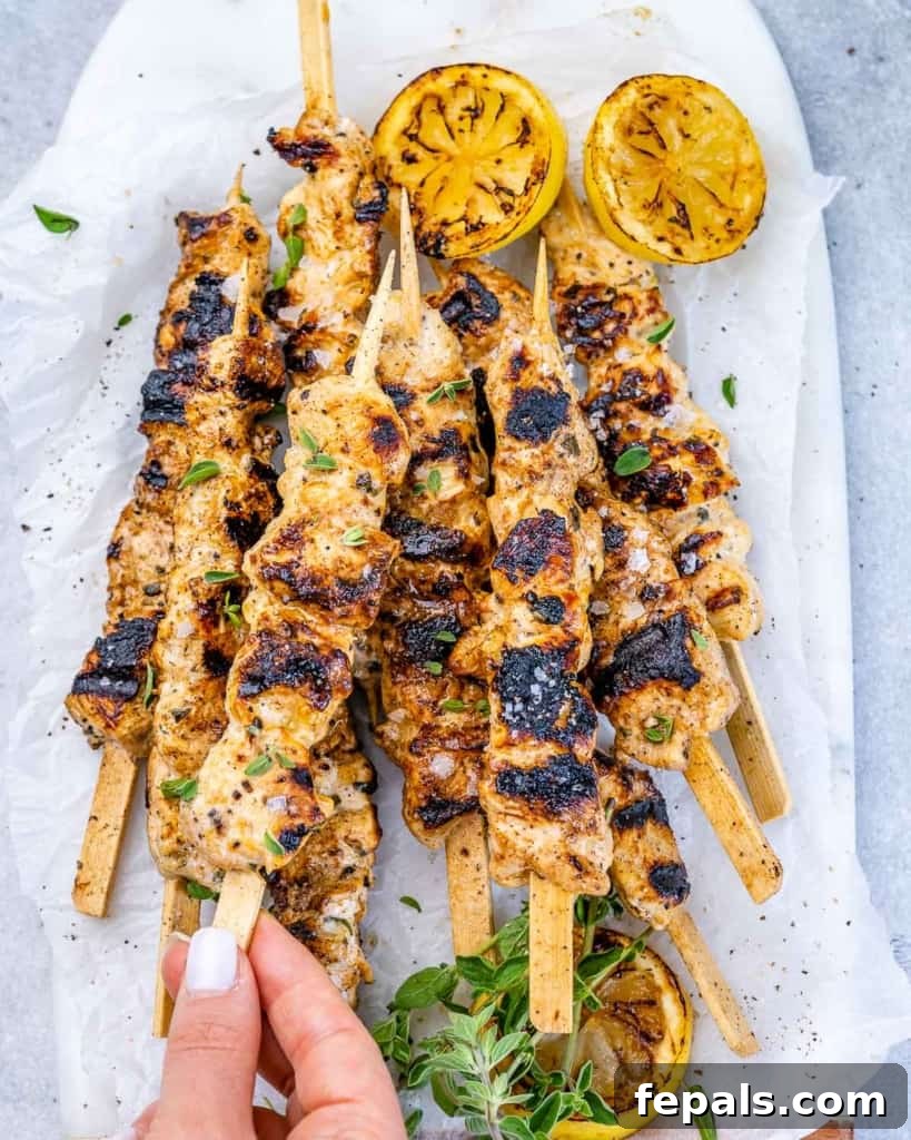grilled lemon chicken skewers on top of white surface with fresh lemon slices