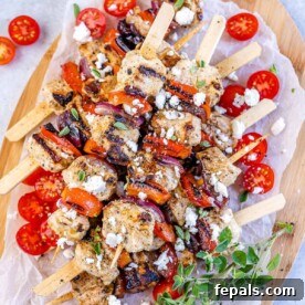 top view chicken skewers with tomato garnishes and feta cheese on a brown cutting board