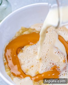 Milk being added to the peanut butter and banana mixture, with oats and chia seeds ready to be stirred in.