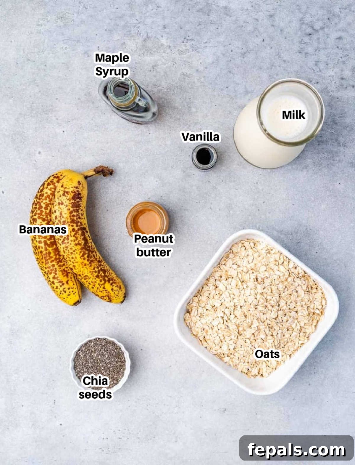 A collection of ingredients laid out, including bananas, peanut butter, maple syrup, vanilla extract, milk, oats, and chia seeds.