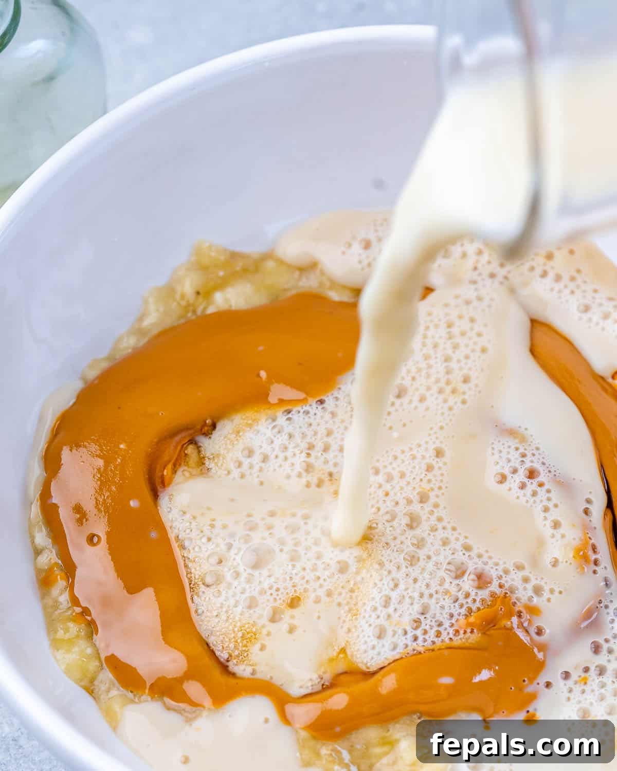 Almond milk being poured into a bowl containing the mashed banana and peanut butter mixture.