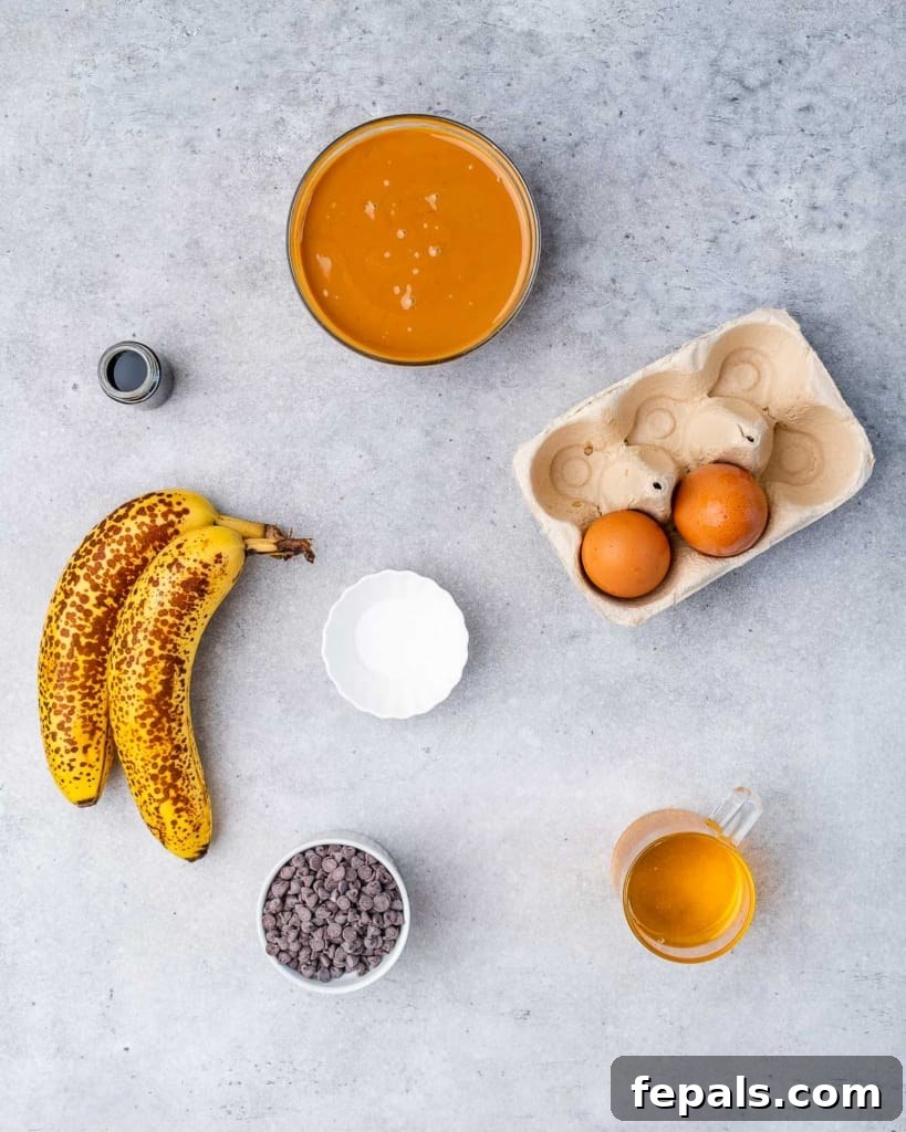 Wholesome Flourless Peanut Butter Banana Muffins 4 A collection of ingredients laid out in bowls, ready to make banana muffins. Ingredients include two ripe bananas, a bowl of dark chocolate chips, two eggs, a bowl of creamy peanut butter, maple syrup, vanilla extract, and baking soda.