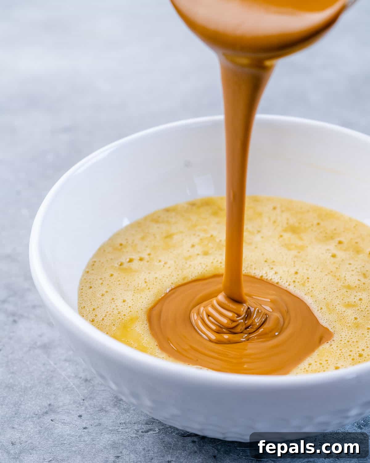 Wholesome Flourless Peanut Butter Banana Muffins 5 Creamy peanut butter being poured over a bowl of mashed bananas, ready to be mixed into a delicious muffin batter.