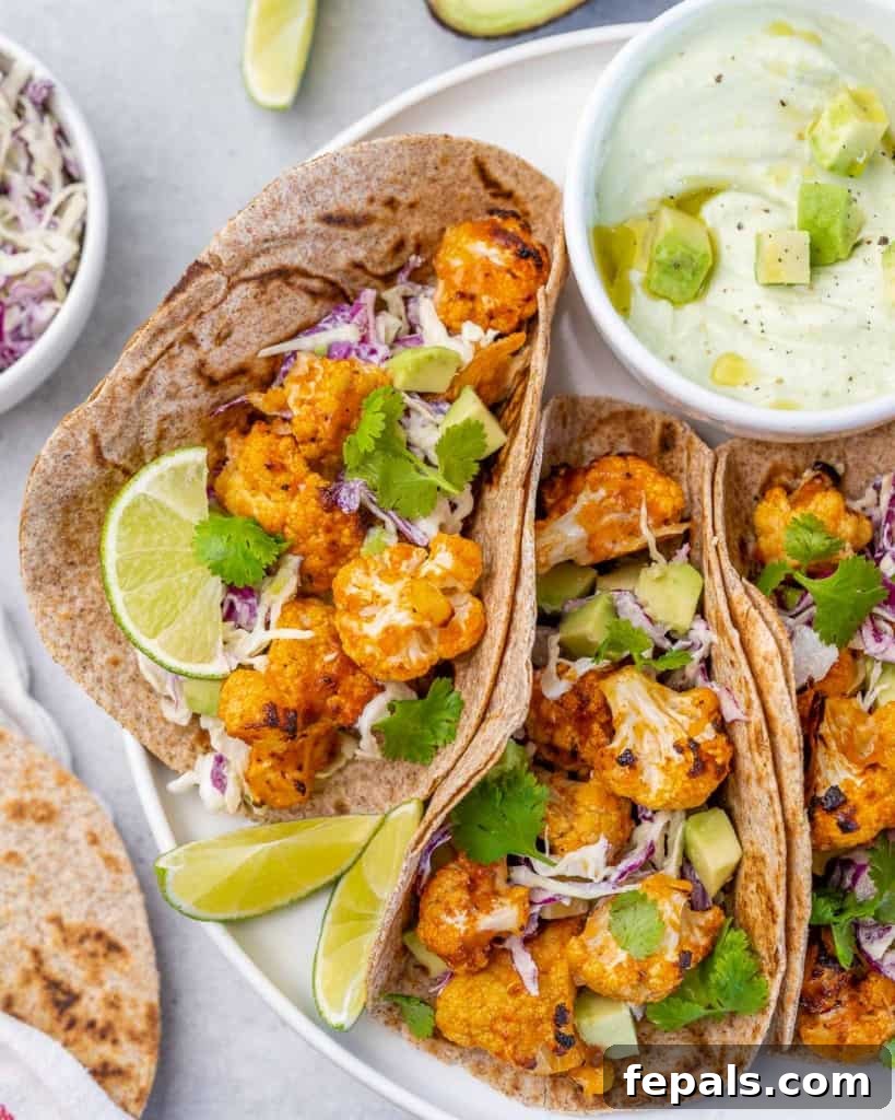 Side view of a single cauliflower taco, artfully garnished, positioned on a white plate with a side of creamy yogurt dip, emphasizing its fresh ingredients.