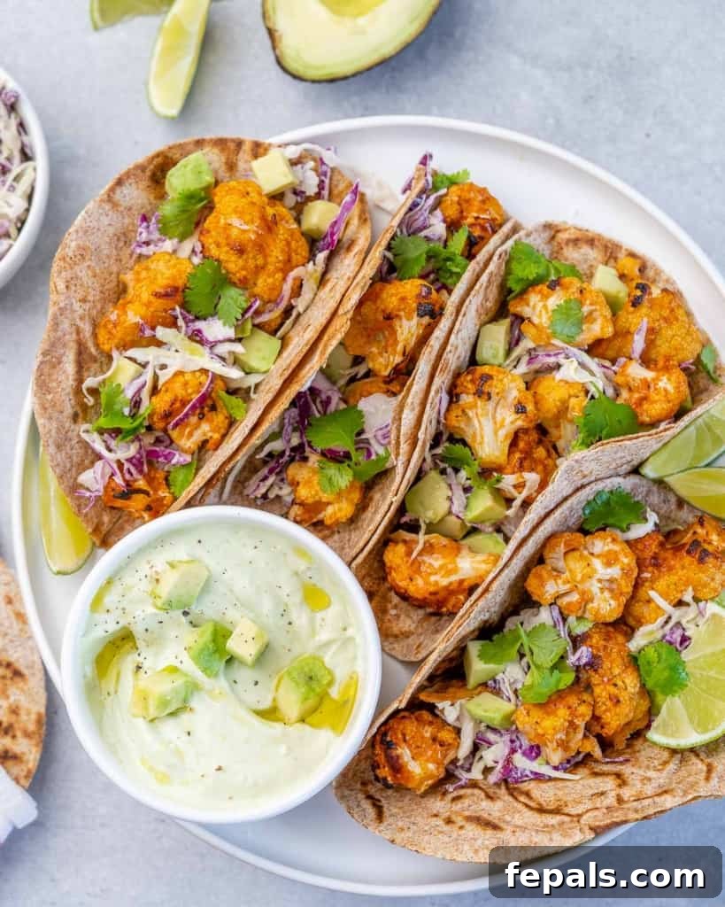 Close-up top view of a single cauliflower taco, generously filled and garnished, with a dollop of avocado yogurt sauce on the side.
