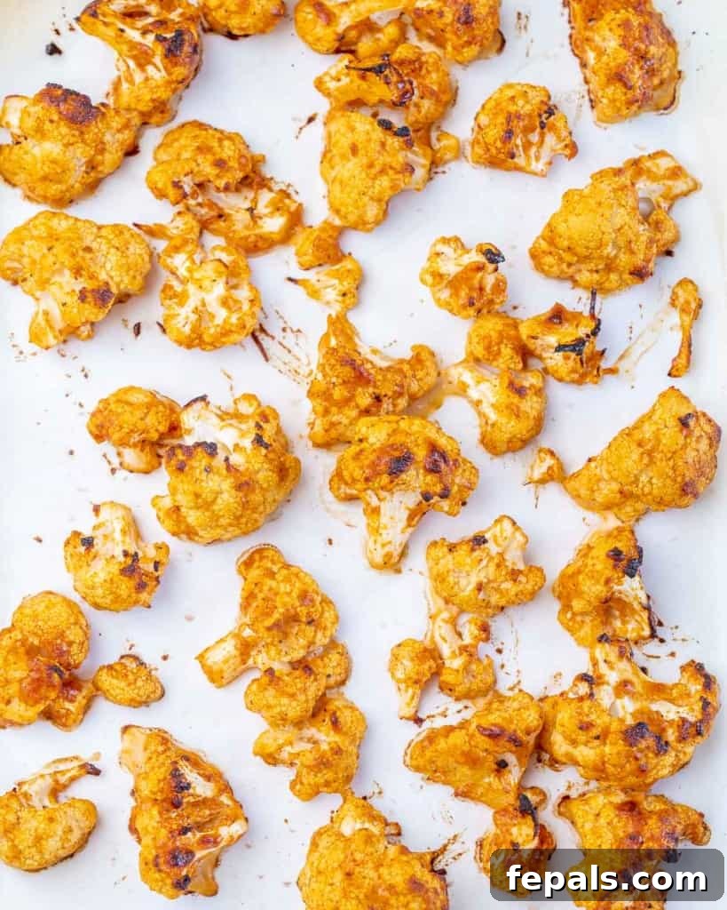 Freshly baked cauliflower florets, golden brown and crispy, spread out on a parchment-lined baking sheet.