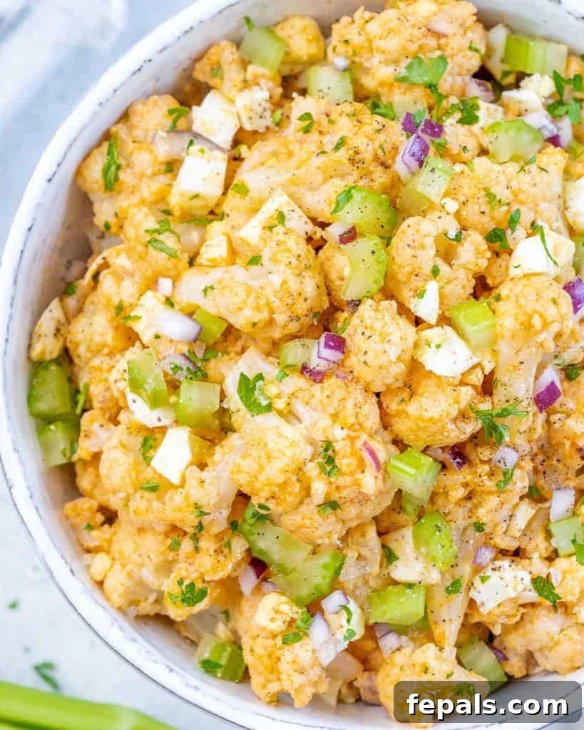 Cauliflower Mock Potato Salad 7 Healthy cauliflower potato salad in a white bowl, ready to be served, garnished with fresh herbs.