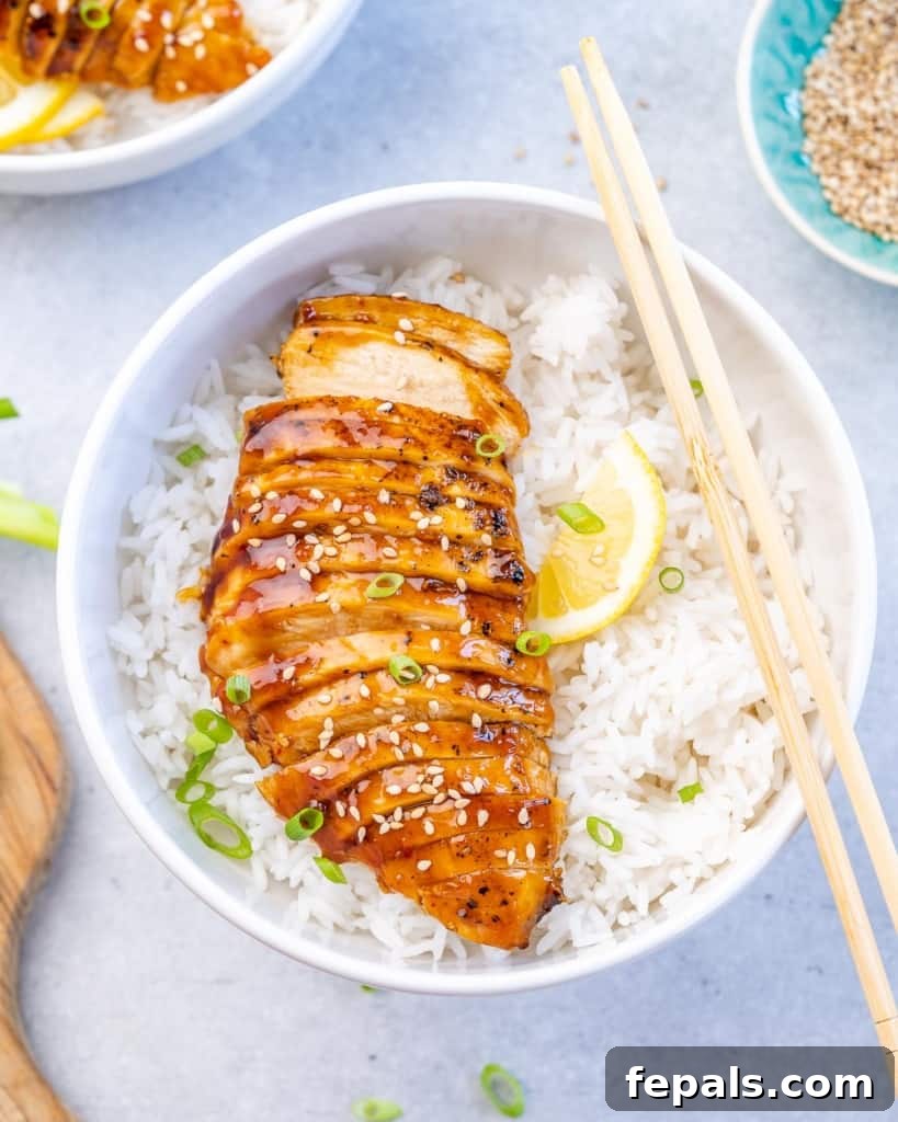 Top view of perfectly sliced baked teriyaki chicken breast, glistening with sauce, served over a bowl of steamy white rice, ready to be enjoyed.
