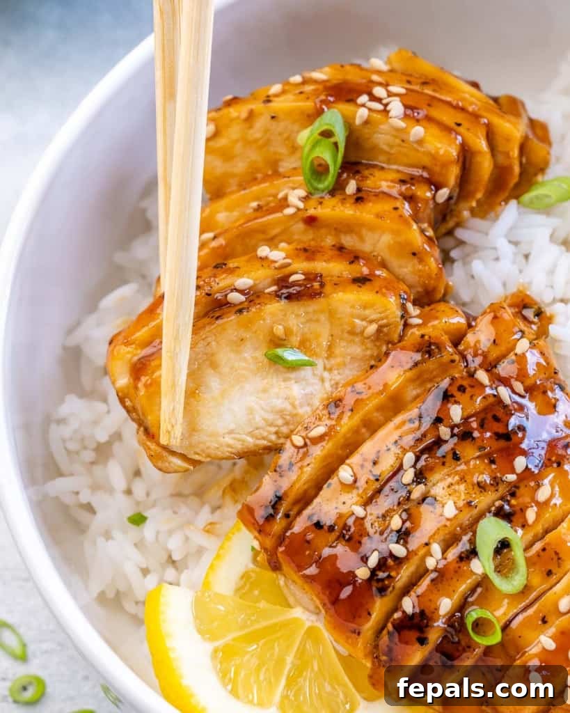 Close-up shot of chopsticks delicately holding a piece of perfectly sliced, saucy teriyaki chicken, showcasing its tender texture and rich glaze.